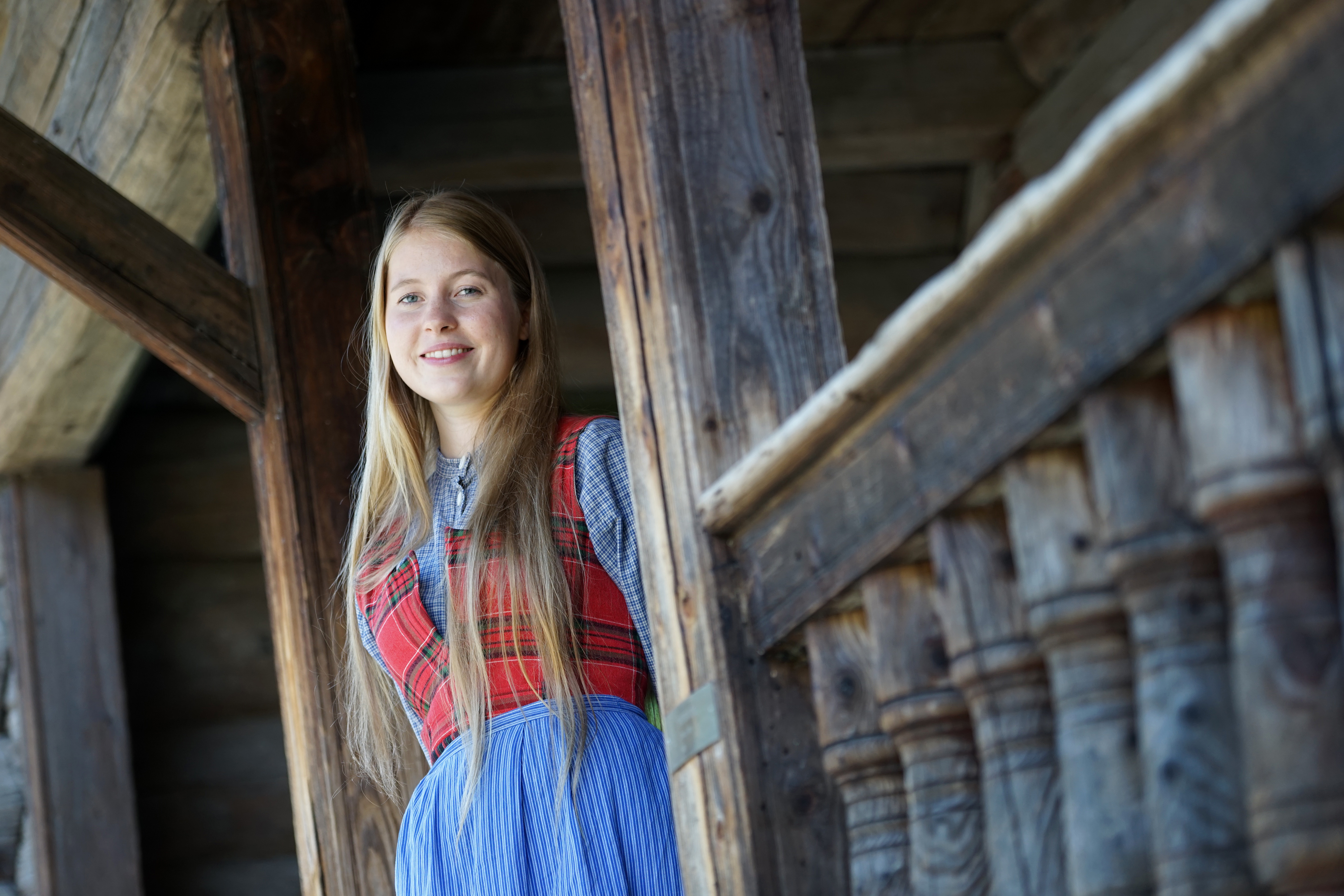 Young woman in traditional dress by a timber building at Maihaugen.