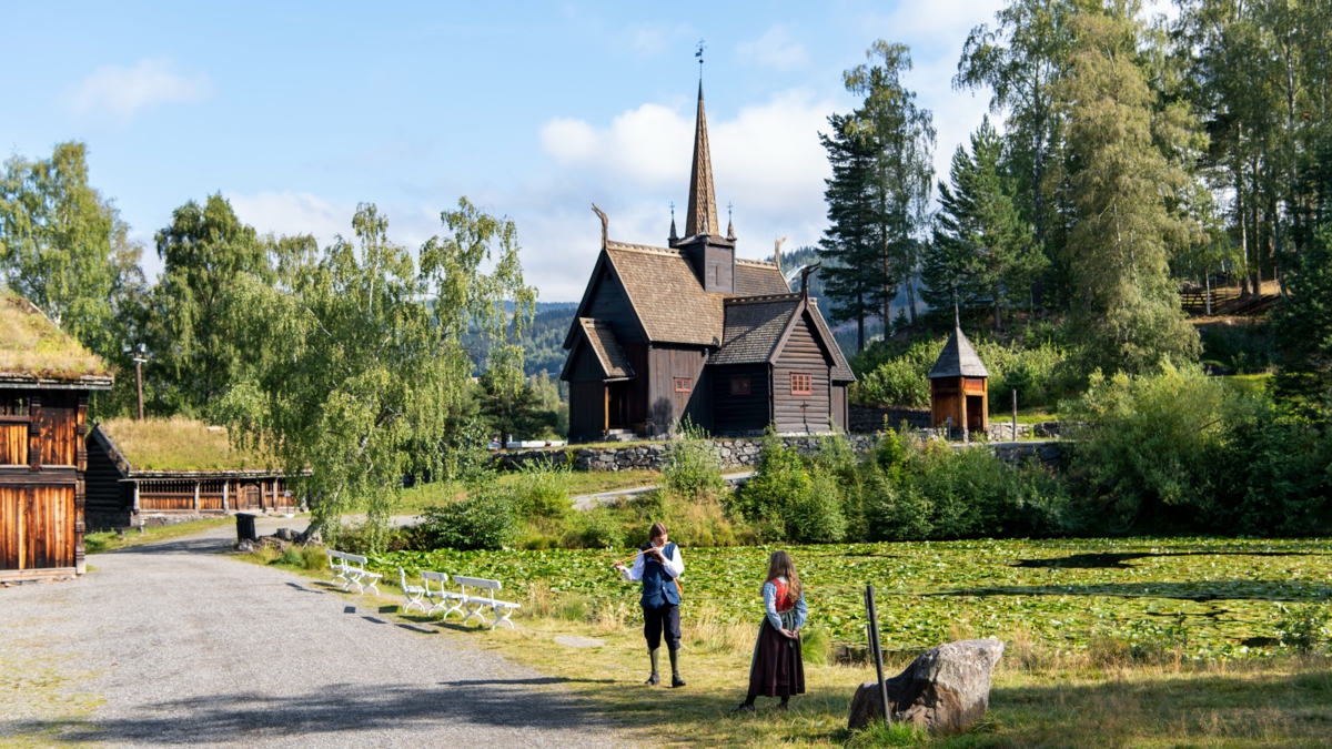 Garmo Stavkirke med gutt og jente i bunad som skiller på et instrument