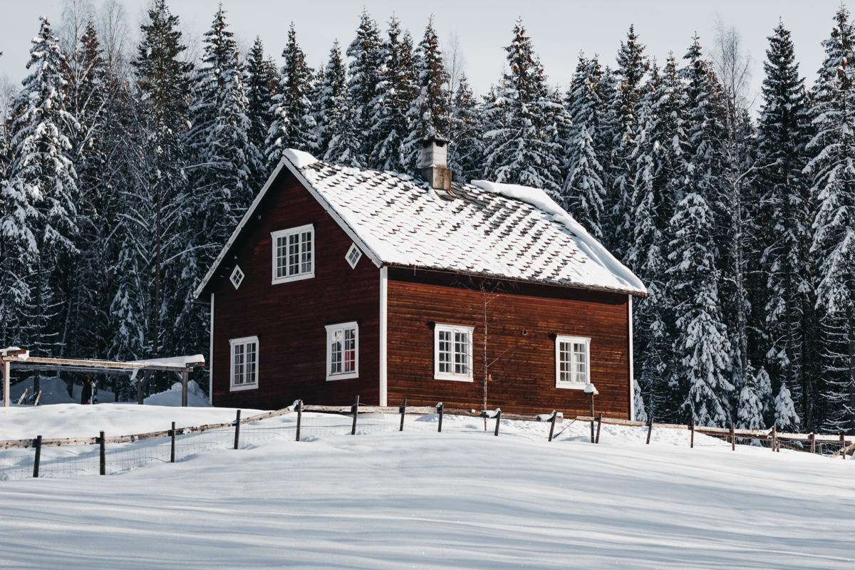 Rødmalt hus i skogkanten i vinterlandskap.