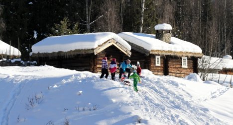 Barn aker foran gammelt tømmerhus på Maihaugen i Lillehammer.